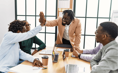 Group of professionals around a table, two are exchanging a high-five.