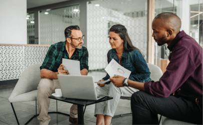 3 business professionals gathered around a laptop and reviewing documents