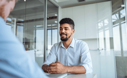 man smiling and sitting with elbows on table in the middle of interview