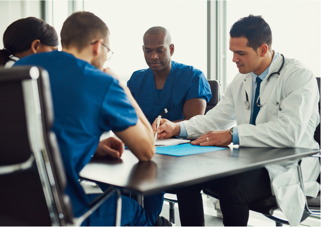 group of four healthcare leaders in scrubs and lab coats in a meeting and reviewing a document