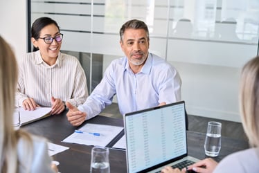 two business professionals sitting at desk talking to a colleague