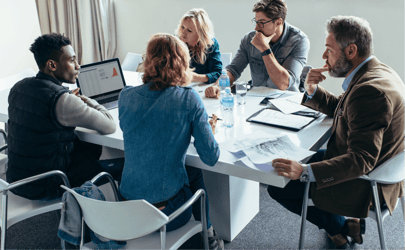 5 business professionals sitting at table reviewing a report on laptop