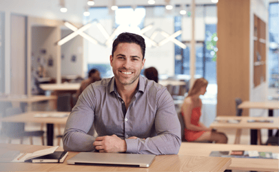 man sitting at desk with closed laptop and smiling 