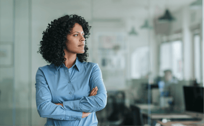 woman with curly hair in blur shirt looking off into distance with arms crossed