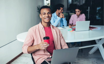 Professional smiling while holding coffee and working at their computer.