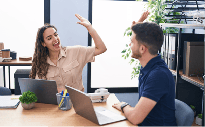 woman and man sitting and high-fiving each other with laptops open in front of them