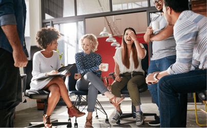 6 diverse office workers sitting and gathered around each other laughing in a meeting