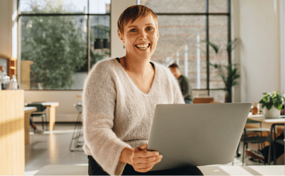 woman sitting down smiling while holding an open laptop
