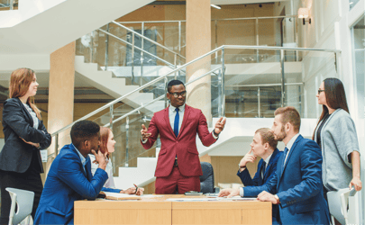 man in red business suit leading a meeting and talking to four colleagues 