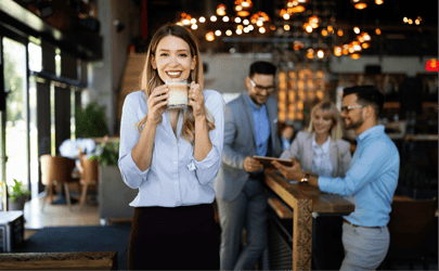 business woman smiling with coffee mug and three colleagues behind her reviewing a document