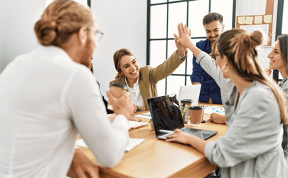 Group of business professionals sitting around table, two are exchanging high-fives.