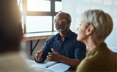 man in glasses explaining something and speaking to a group in the foreground with his hands out