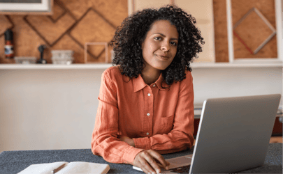 female executive in orange shirt working at laptop with her hand on the trackpad