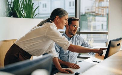 business woman showing associate something on a computer screen that they're both looking at