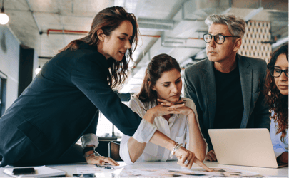 female business leader pointing to paper on desk with two colleagues paying attention