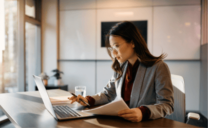 business woman sitting down at laptop with documents in her hand