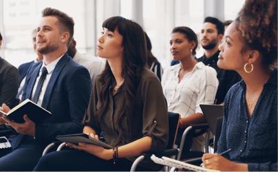 group of diverse professionals sitting down in an audience and listening to a speaker out-of-frame