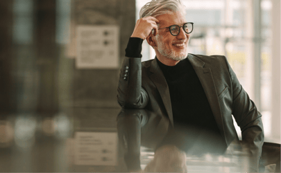 business man leaning against table while smiling and looking into distance