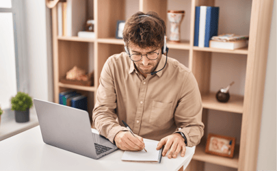 man with headset writing on a notepad