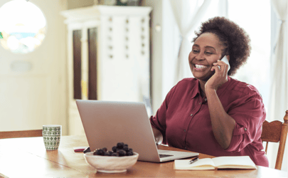 woman smiling on phone and laptop open in front of her