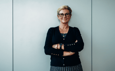 woman with glasses leaning against wall with arms crossed