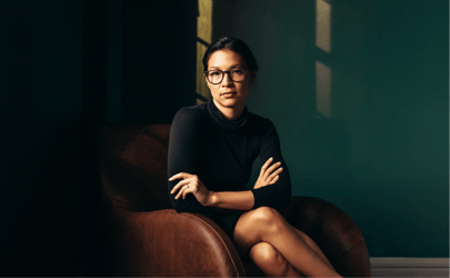 woman in a dark room sitting on a chair with arms crossed