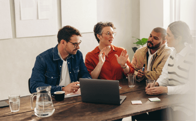 group of 4 professionals discussing something with an open laptop on table