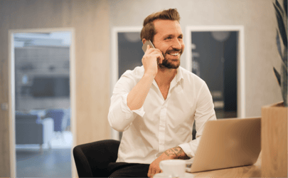 man sitting at desk on the phone with an open laptop in front of him