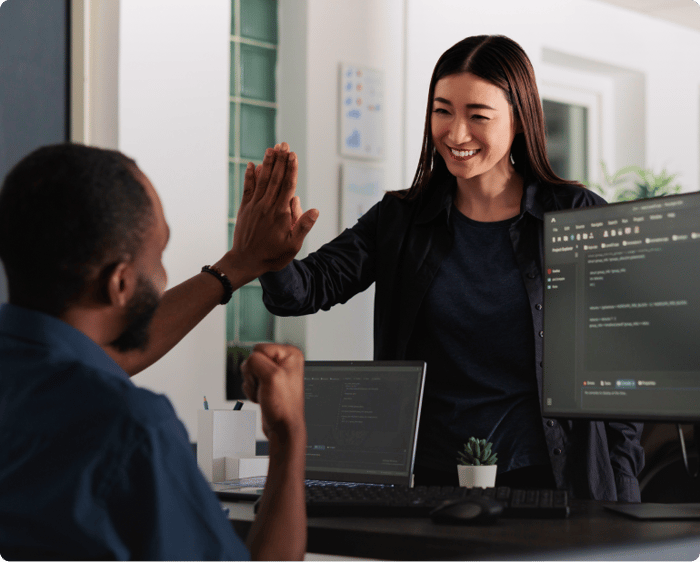 woman high-fiving man in front of two computer screens with code on them