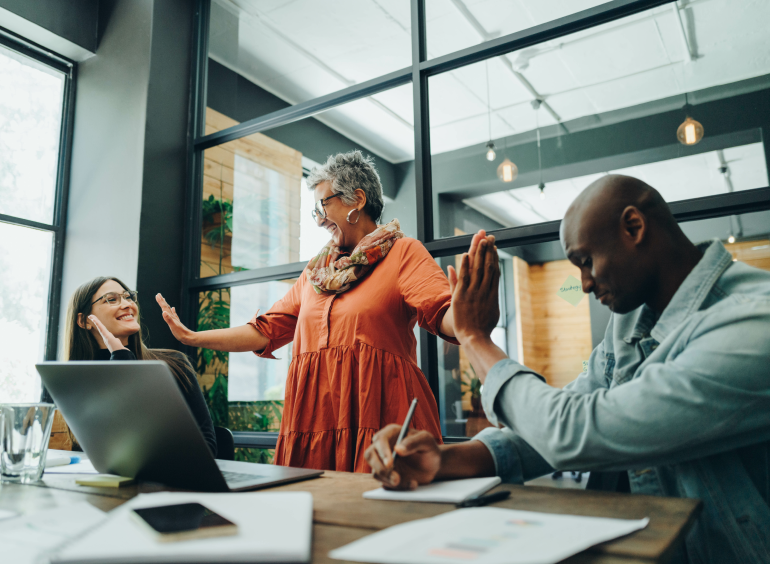 woman in orange dress high-fiving two colleagues on each side