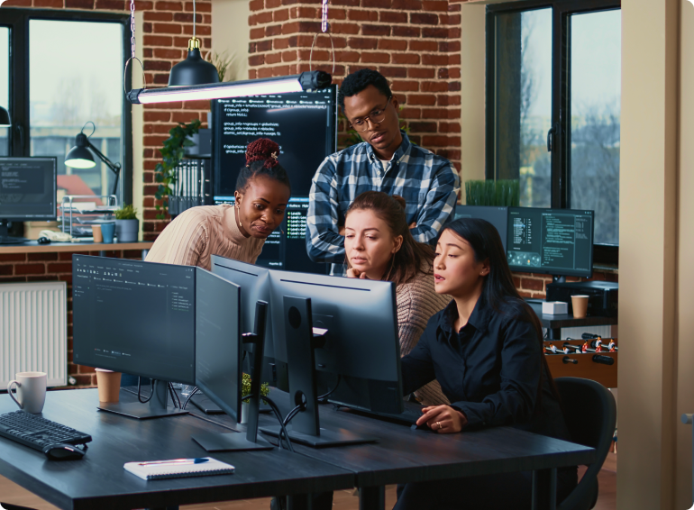 group of four engineers gathered around computers with code on screen and solving a problem