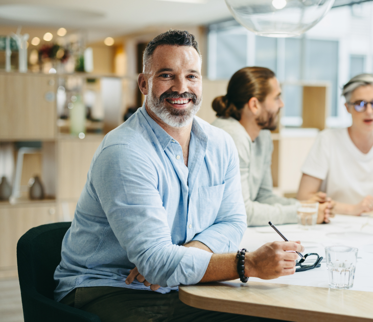 man smiling and sitting down at desk with pencil in hand