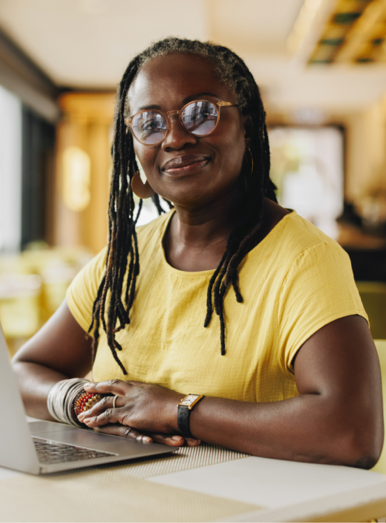 Woman in glasses, smiling to the camera from her desk.