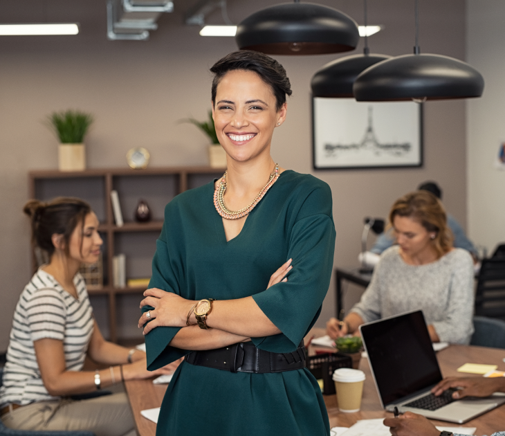 woman smiling with arms crossed and standing in front of two colleagues in background