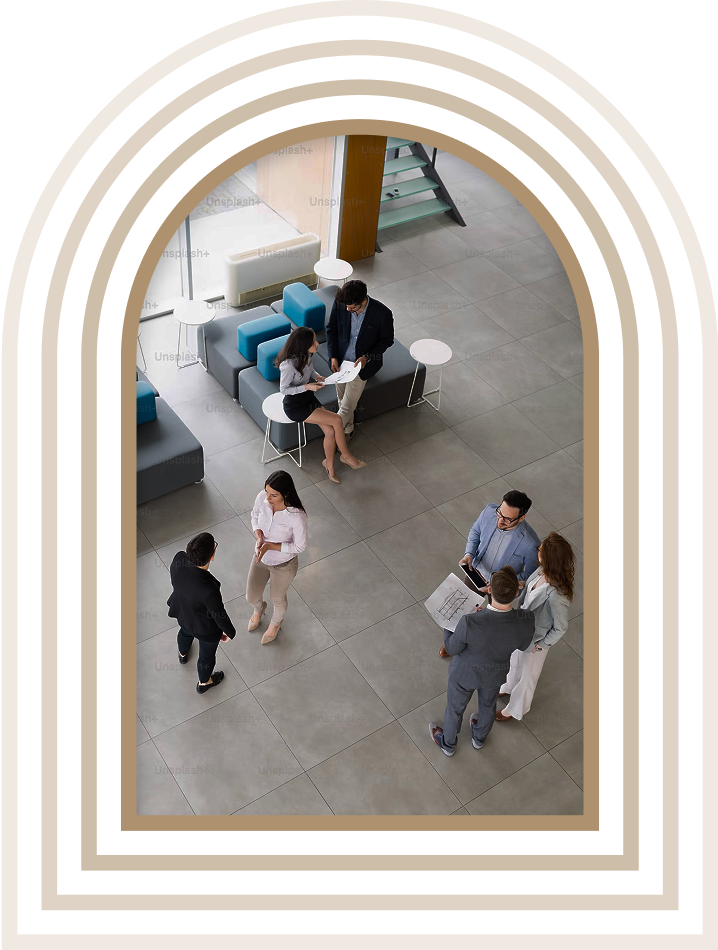 Group of business professionals having conversations and reviewing documents in a modern office lobby, viewed from above through an arched frame design.