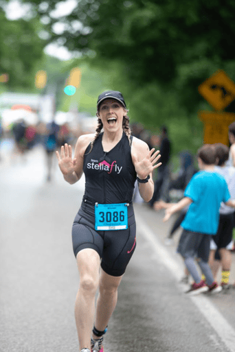 Candid shot of Hunt Club’s Customer Success Manager, Elyse Mathos, running in a 5k marathon and holding her hands out smiling