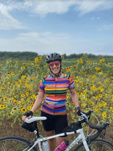 Hunt Club’s Customer Success Manager, Elyse Mathos, smiling while holding her mountain bike on a trail in front of sunflowers