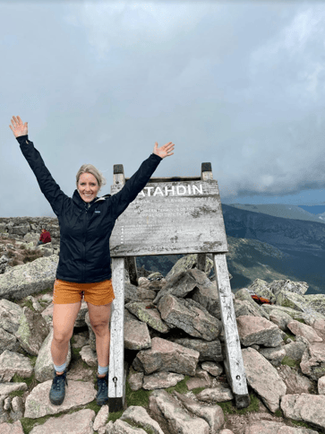 Hunt Club’s Customer Success Manager, Elyse Mathos, standing triumphantly with her arms up on top of a mountain