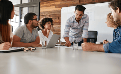 group of 5 colleagues meeting and sitting at a table with an open laptop